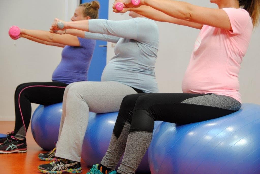 Drie zwangere vrouwen trainen met gewichten op fitnessballen
